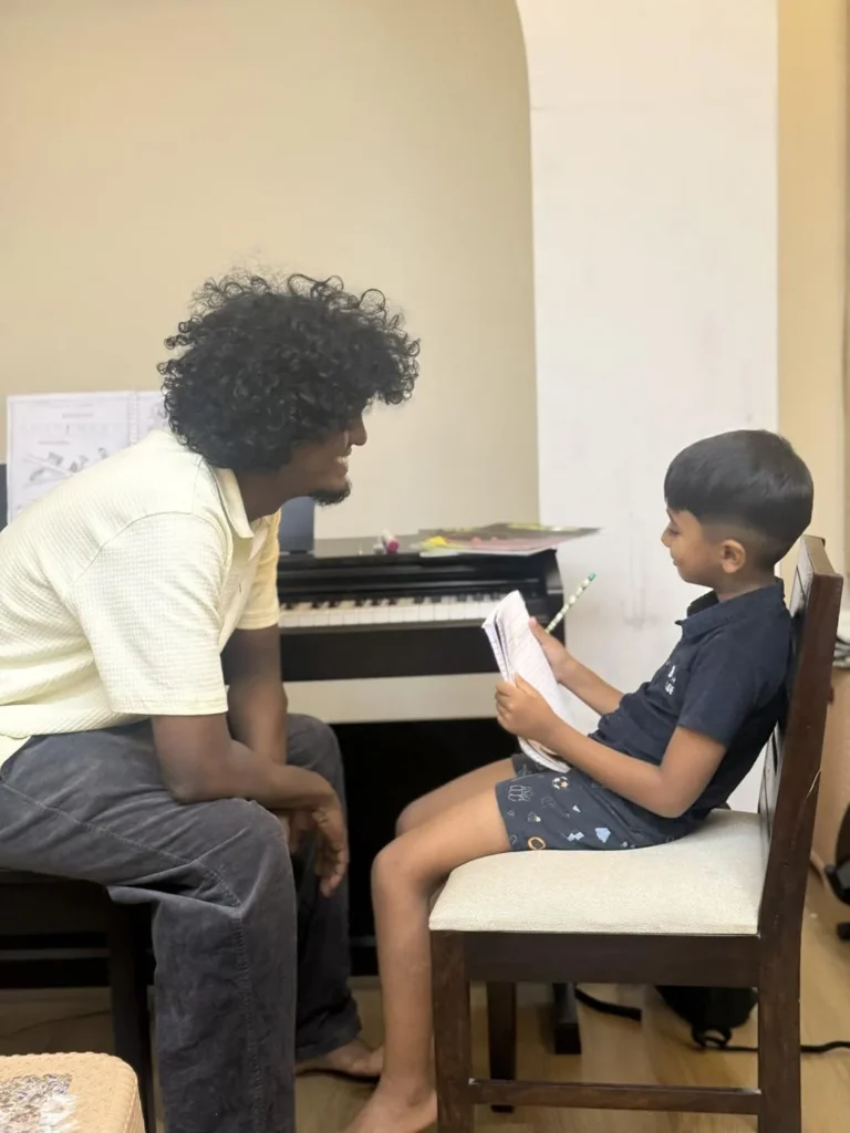 A Shelter teacher guiding a young student through his book at the piano