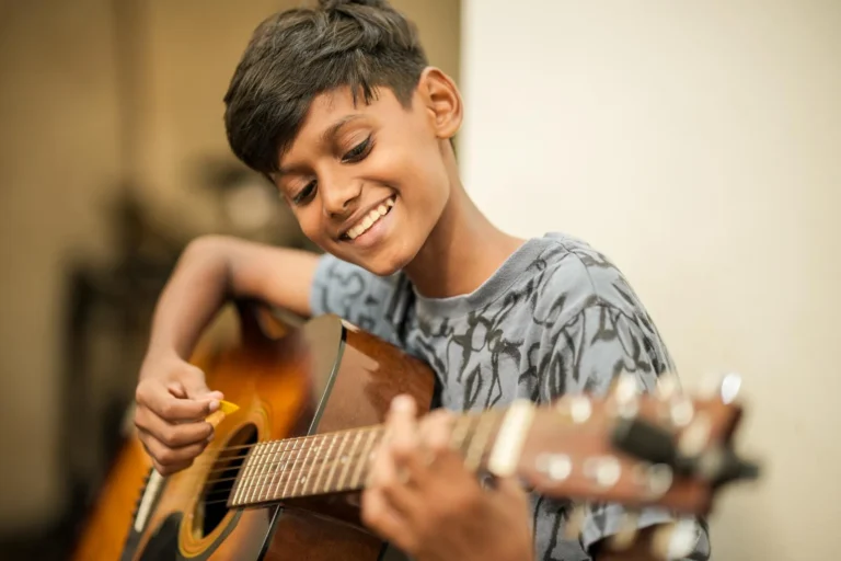 A young student smiling as he plays guitar